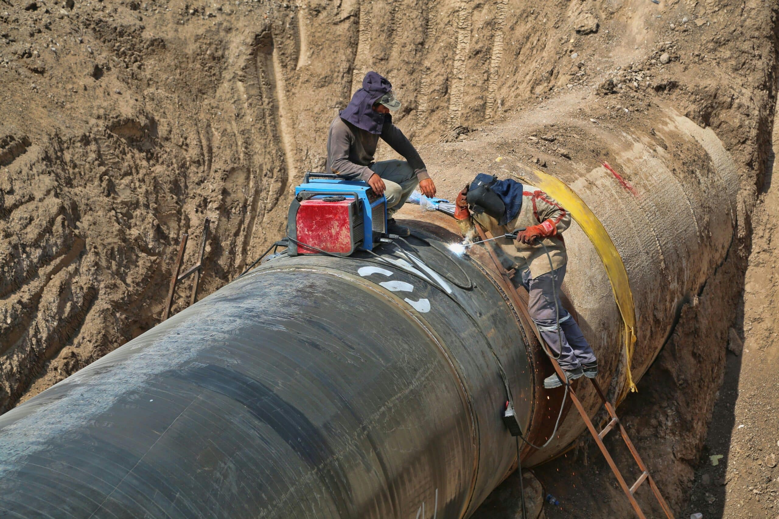 Workers welding an industrial pipeline in a trench